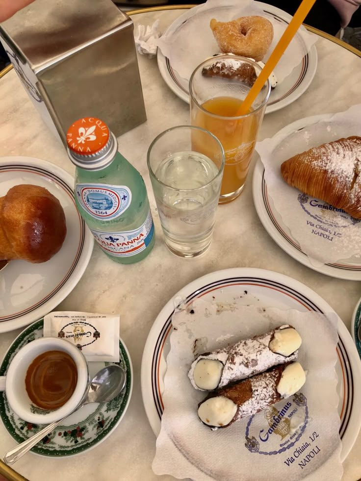 a table topped with plates filled with pastries and desserts next to drinks on saucers