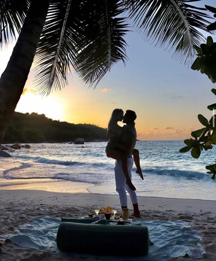 a man and woman kissing on the beach at sunset