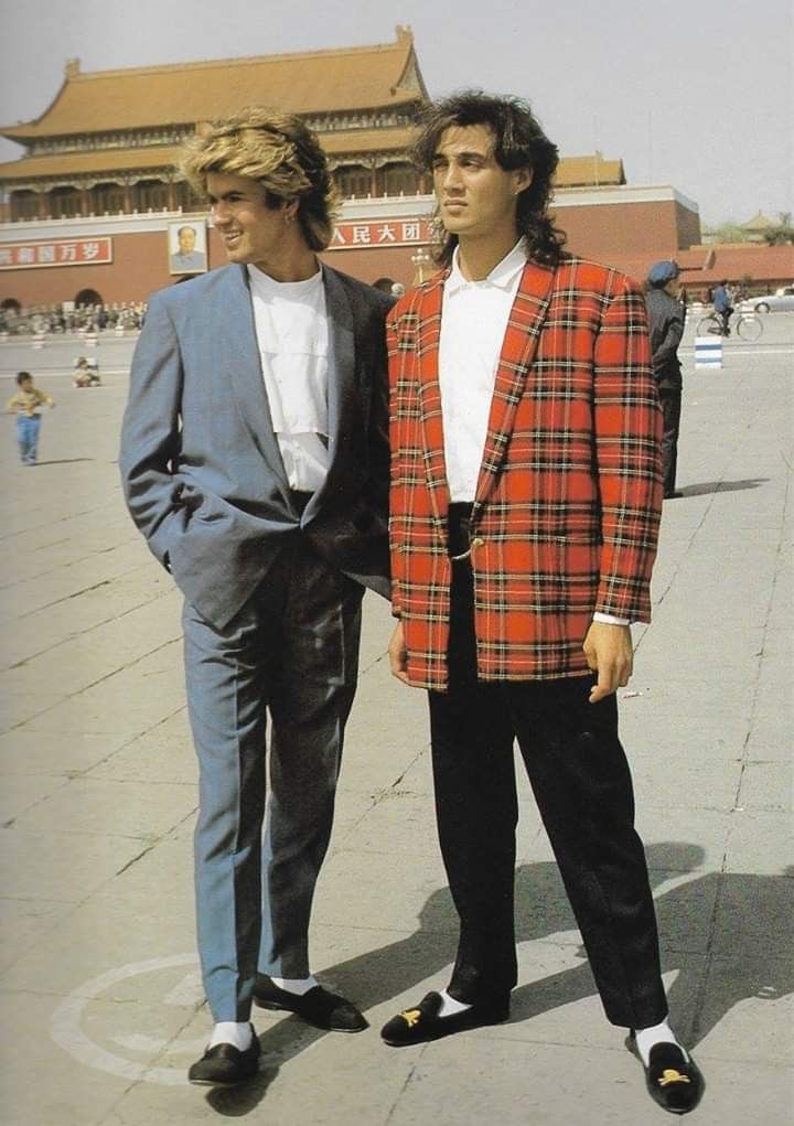 two men standing next to each other in front of a building