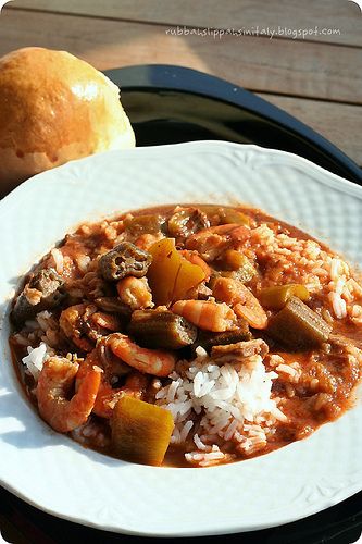 a white plate topped with rice and stew next to a roll on a wooden table