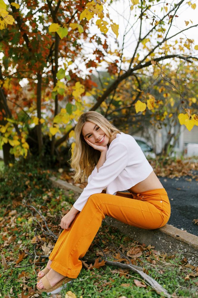 a woman sitting on the ground with her legs crossed and looking at the camera while wearing orange pants