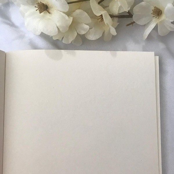 an open book sitting on top of a table next to white flowers and a pen