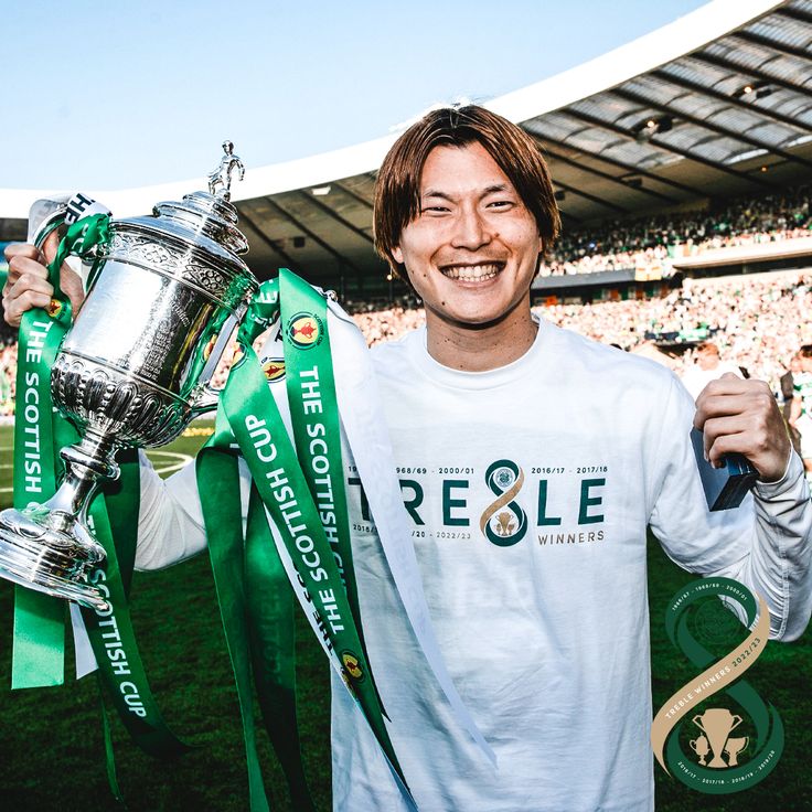 a man holding up a trophy and wearing a green scarf in front of a crowd