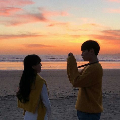 a man and woman standing on top of a beach next to the ocean at sunset