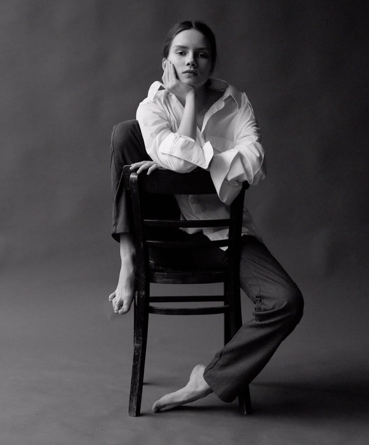 a black and white photo of a woman sitting in a chair with her hands on her chin