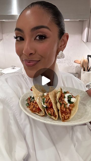 a woman holding a plate with two tacos on it