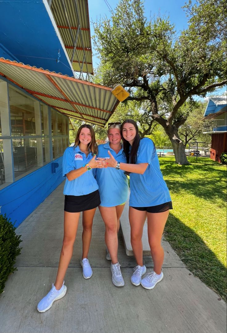 three girls in blue shirts and black shorts posing for the camera with their arms around each other