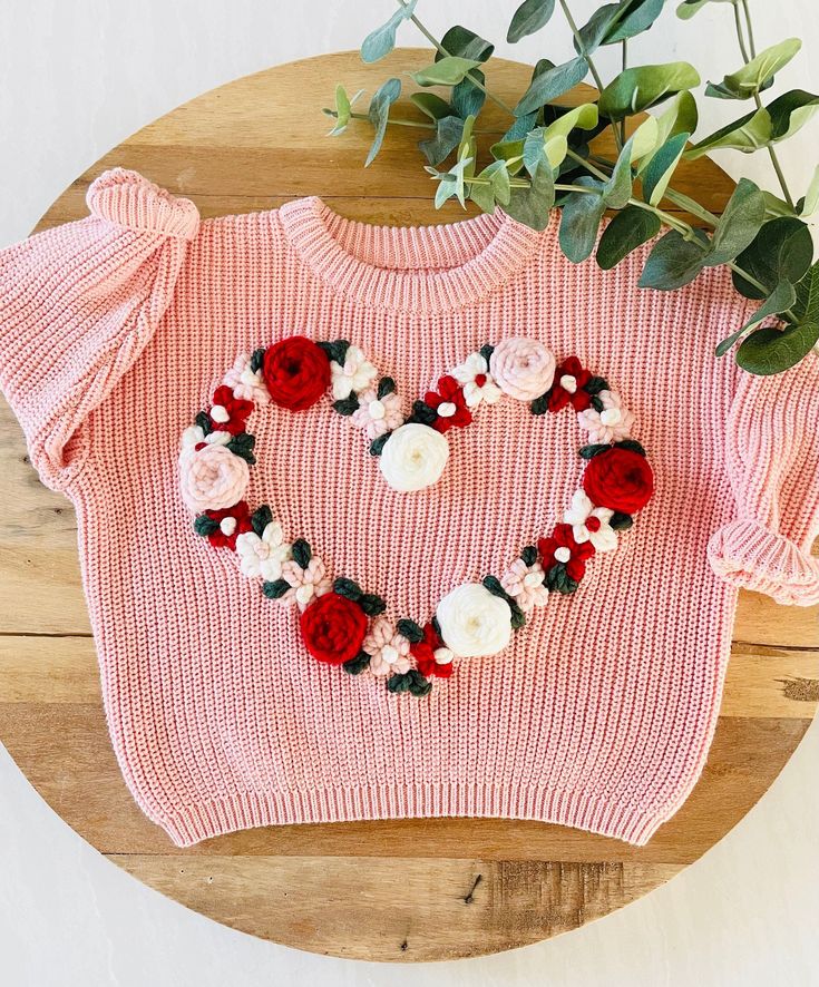 a pink sweater with flowers in the shape of a heart on top of a wooden table