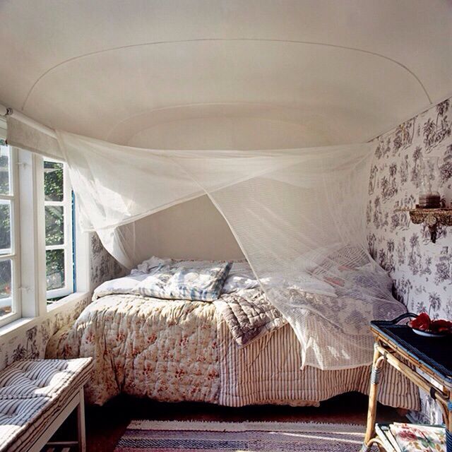 a bed sitting under a white canopy in a bedroom next to a table and chair