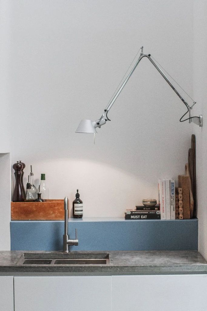 a kitchen sink under a lamp next to a counter top with books and other items on it