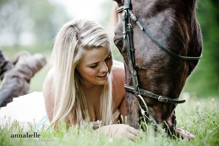 a woman laying in the grass next to a horse