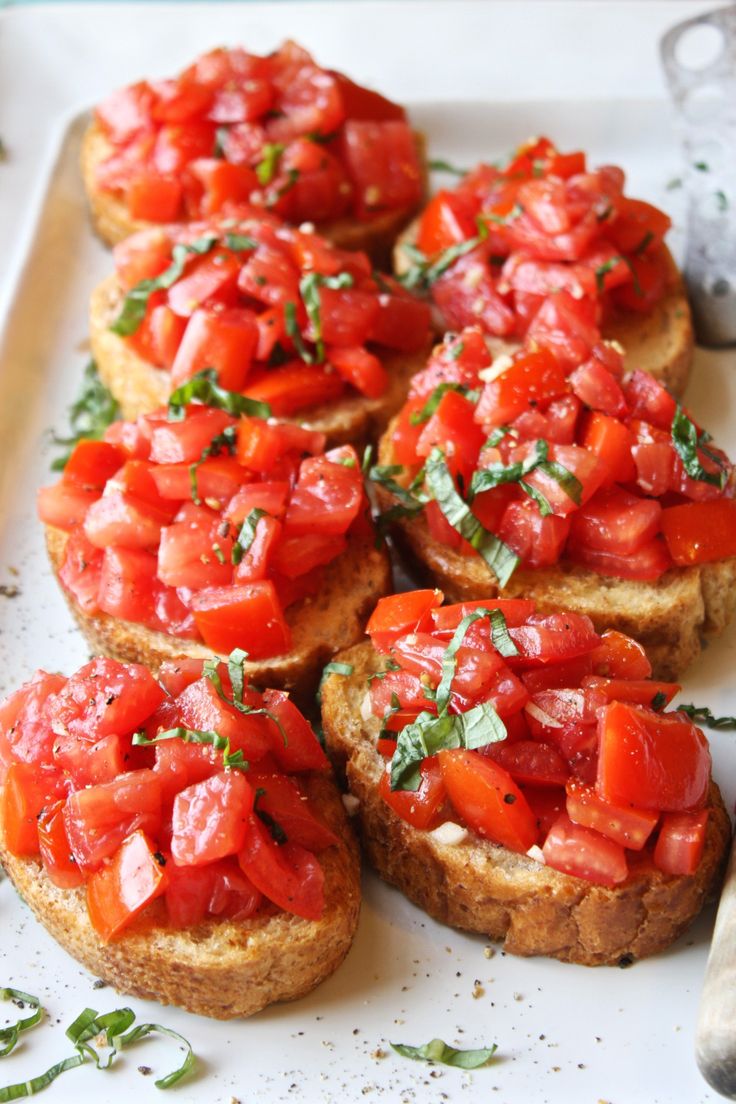 several pieces of bread topped with tomatoes and parsley on a white plate next to a knife