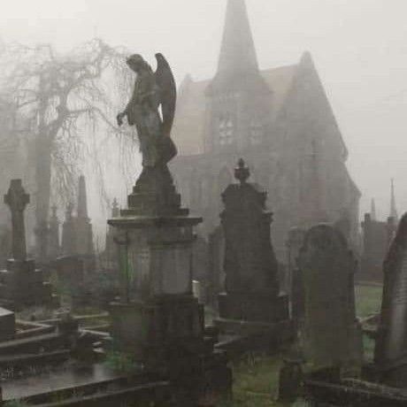 an old cemetery with many headstones and statues in the foreground on a foggy day