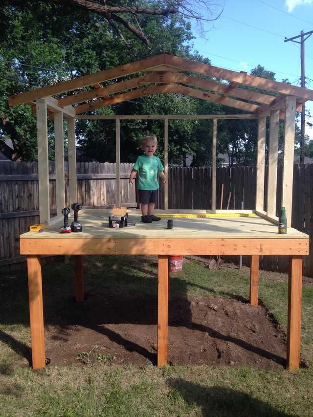 a little boy standing on top of a wooden table in the yard with an umbrella over it