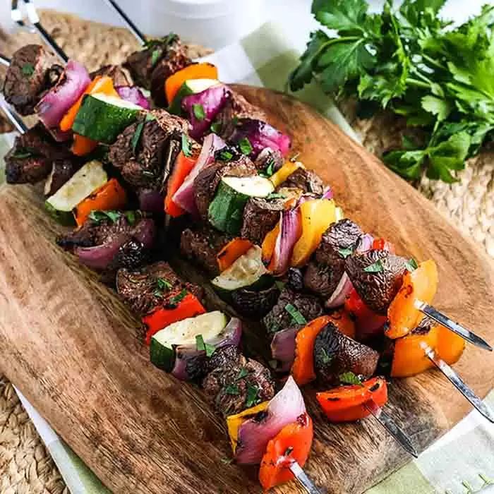 skewers of meat and vegetables on a wooden cutting board next to parsley