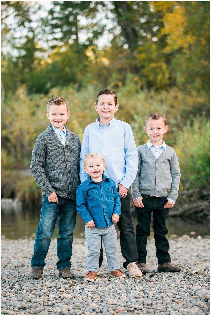 three young boys standing next to each other in front of a body of water and trees