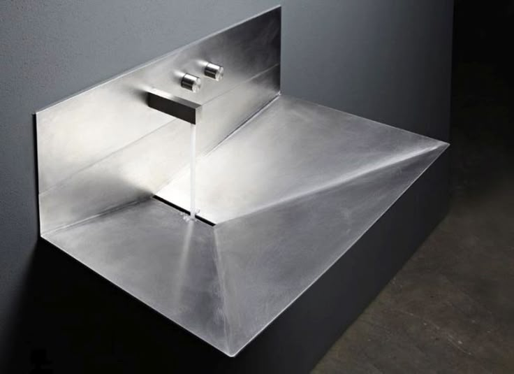 a metal sink mounted to the side of a wall next to a wooden floor and gray walls