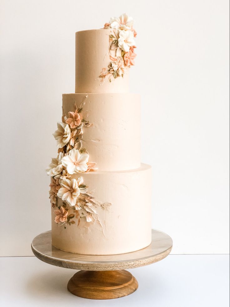 a three tiered white cake with flowers on the top and bottom, sitting on a wooden stand