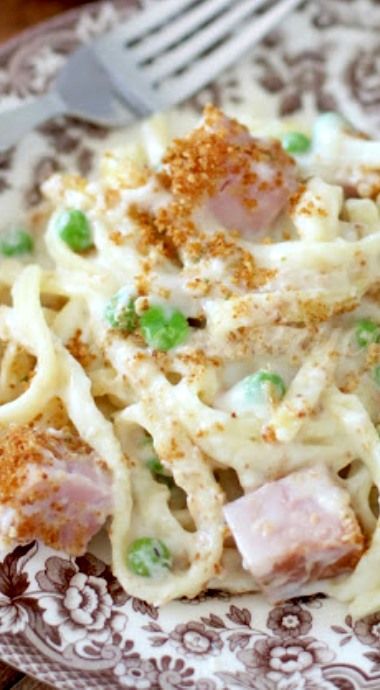 a pasta dish with ham and peas on a brown and white plate next to a fork