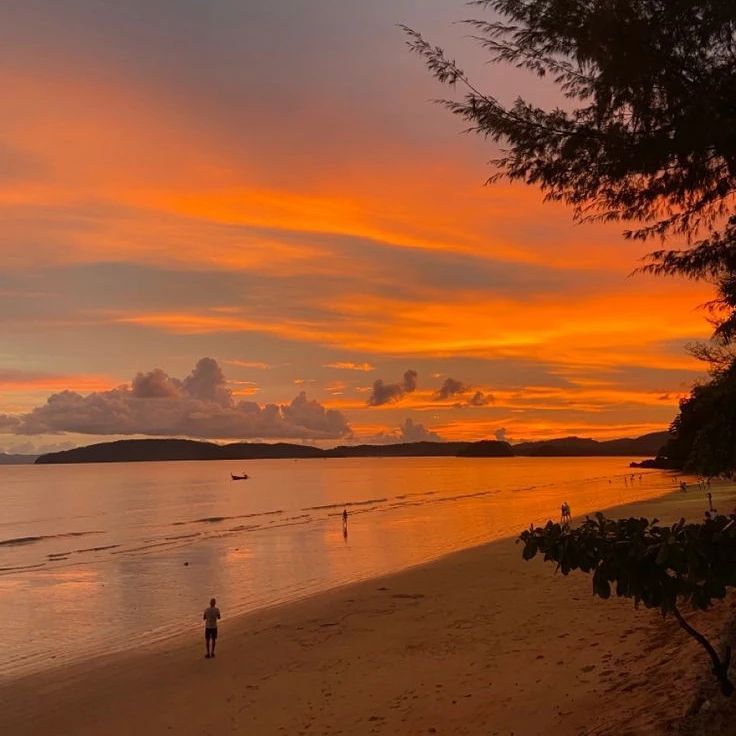 a person is walking on the beach at sunset with boats in the water behind them