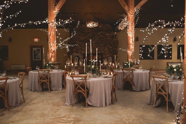 the tables are set up for an event with white flowers and candles on them, surrounded by string lights