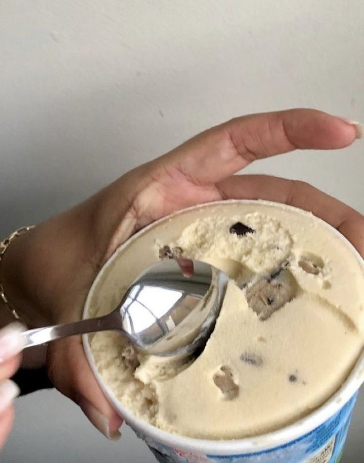 a person holding a spoon in a cup with ice cream and raisins on it