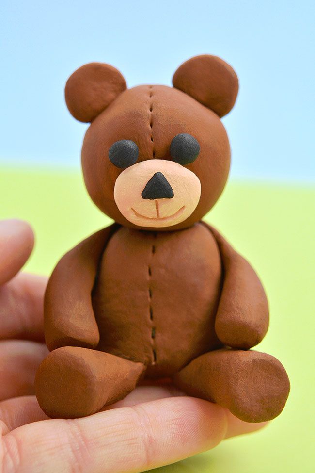 a small brown teddy bear sitting on top of a person's hand in front of a blue and green background