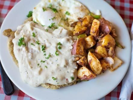 a white plate topped with potatoes and gravy on top of a checkered table cloth