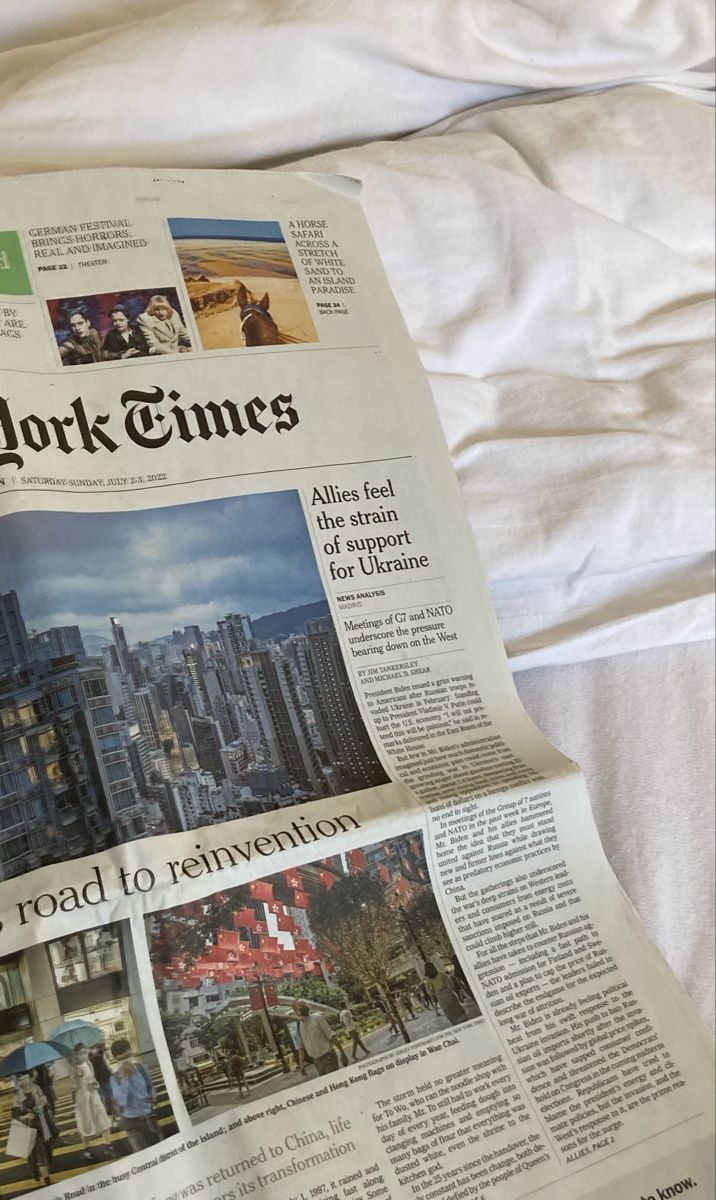 a newspaper laying on top of a bed covered in white sheets and pillows with the new york times front page