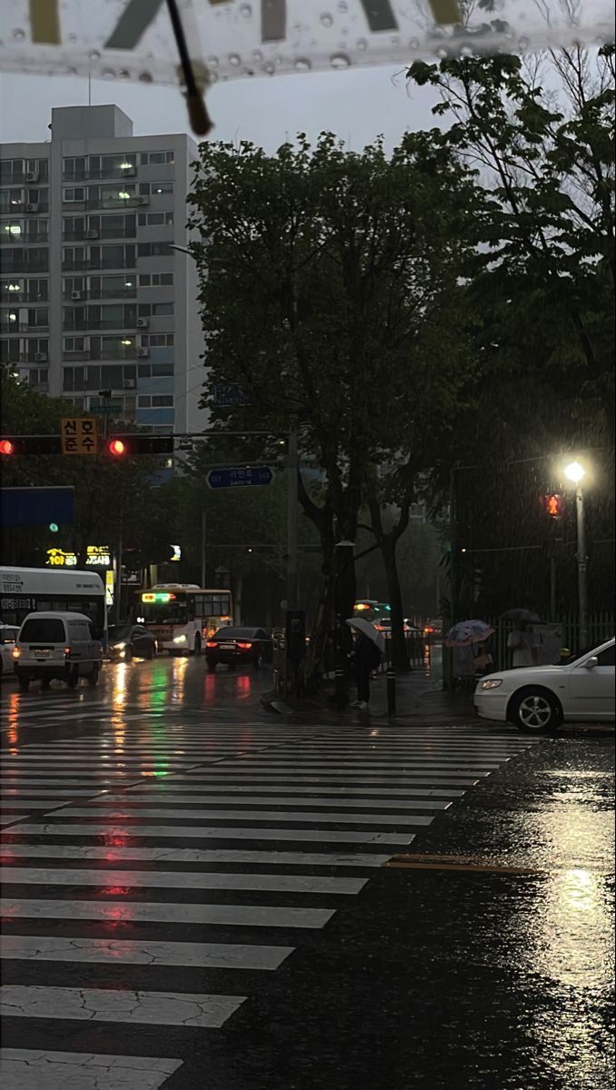 a city street at night with cars driving on the road and people walking across the crosswalk