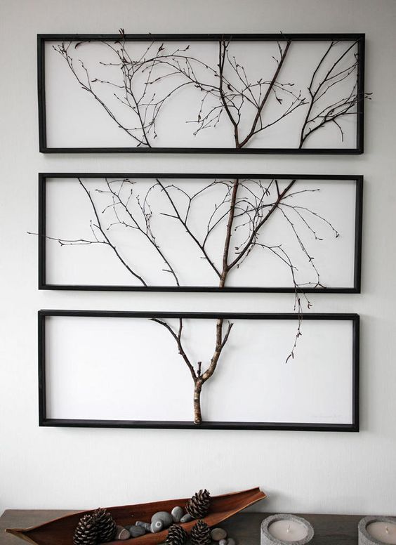 three framed pictures hang on the wall above a table with pine cones and two candles