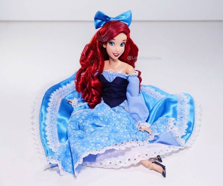 a doll with red hair and blue dress sitting on top of a white tablecloth