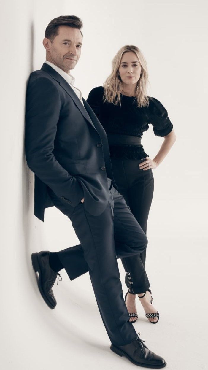 a man and woman posing for a photo in front of a white wall with their hands on the hips