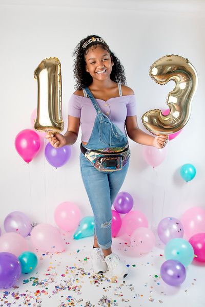 a woman standing in front of balloons holding the number thirteen