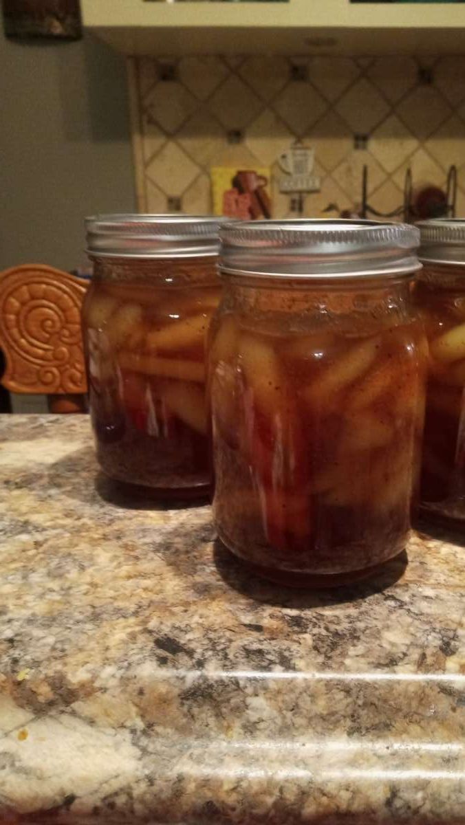 four jars filled with pickled fruit sitting on top of a kitchen counter next to an oven