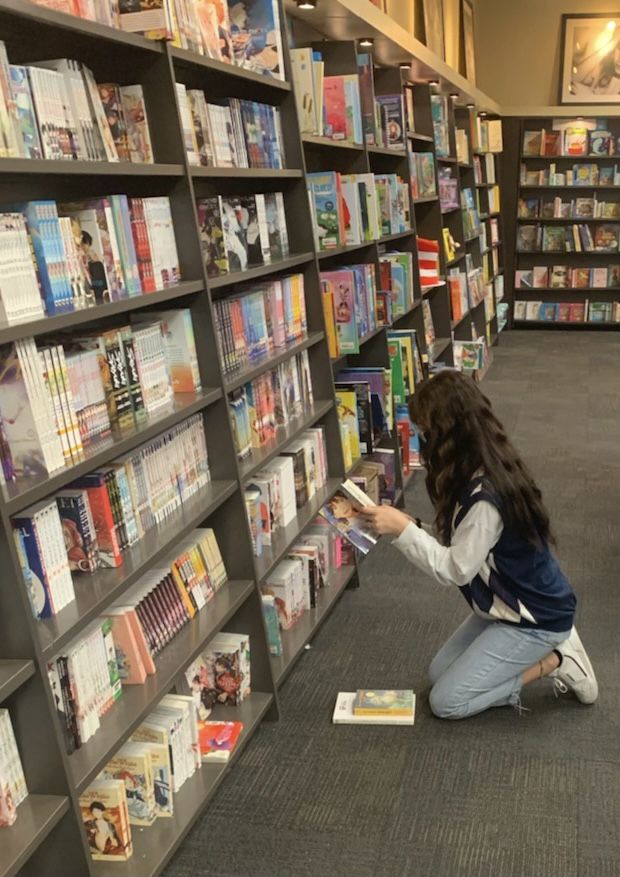 a woman kneeling down in front of a book shelf filled with lots of different books