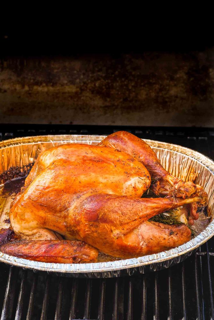 a roasted chicken is on the grill in an aluminum pan, ready to be cooked