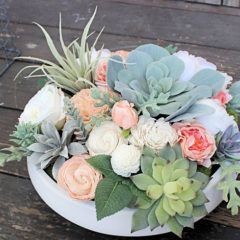 an arrangement of succulents and roses in a white bowl on a wooden table