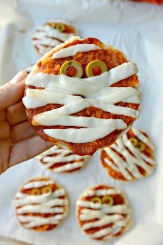 a hand holding a cookie with white icing on it and eyes painted on the top