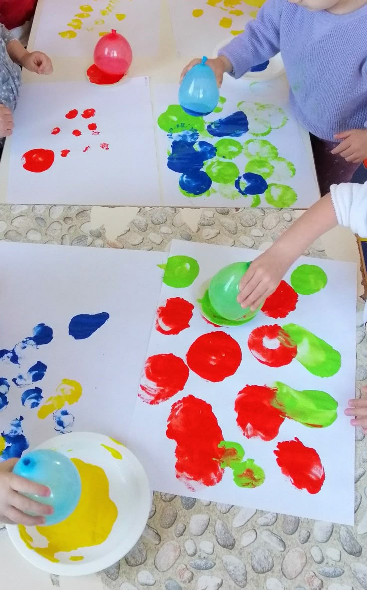 three children are sitting at a table with paper plates and paint on them while one child is painting