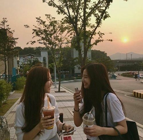 two women standing on the side walk talking to each other while holding drinks in their hands