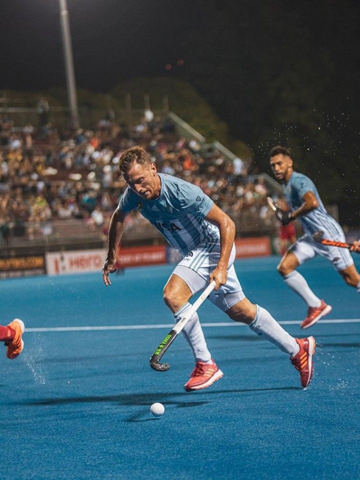 the men are playing a game of field hockey on the blue court in front of an audience