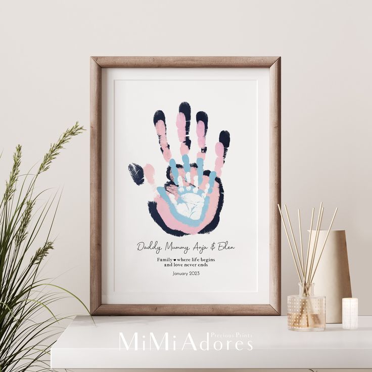 a white shelf topped with a framed print of a pink and blue handprinted baby's hand