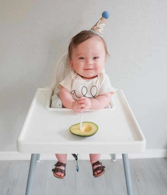 a baby is sitting in a high chair with a birthday hat on and eating an avocado