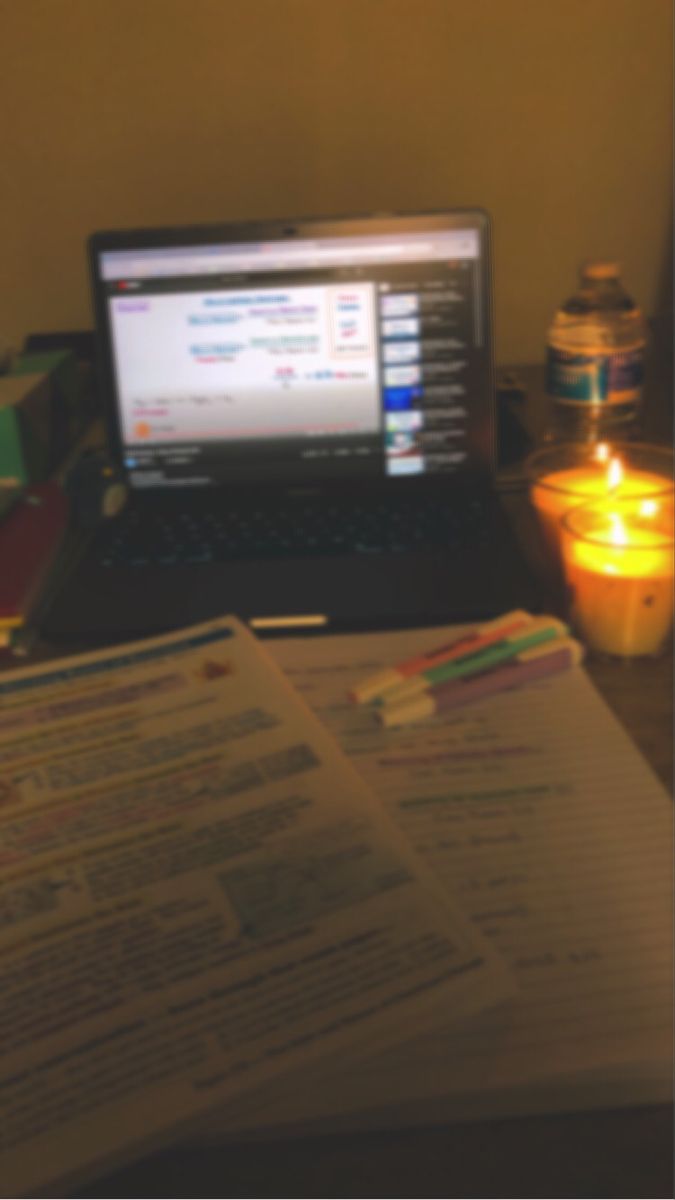 an open laptop computer sitting on top of a desk next to a book and candle