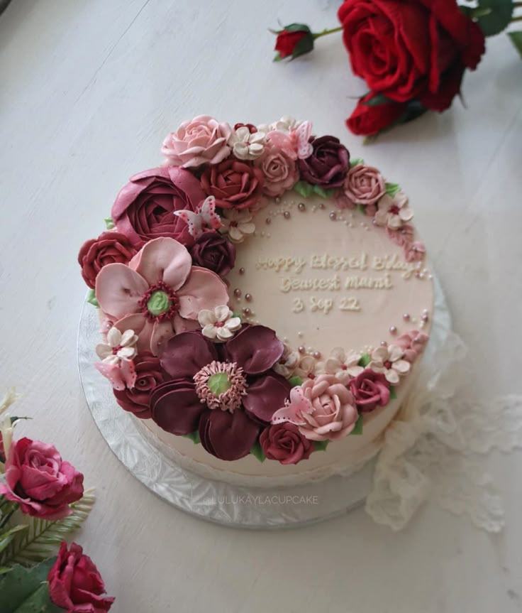 a birthday cake decorated with pink and red flowers on a white table next to roses