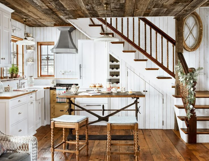 a kitchen with wooden floors and white cabinets, stairs leading up to the upper floor