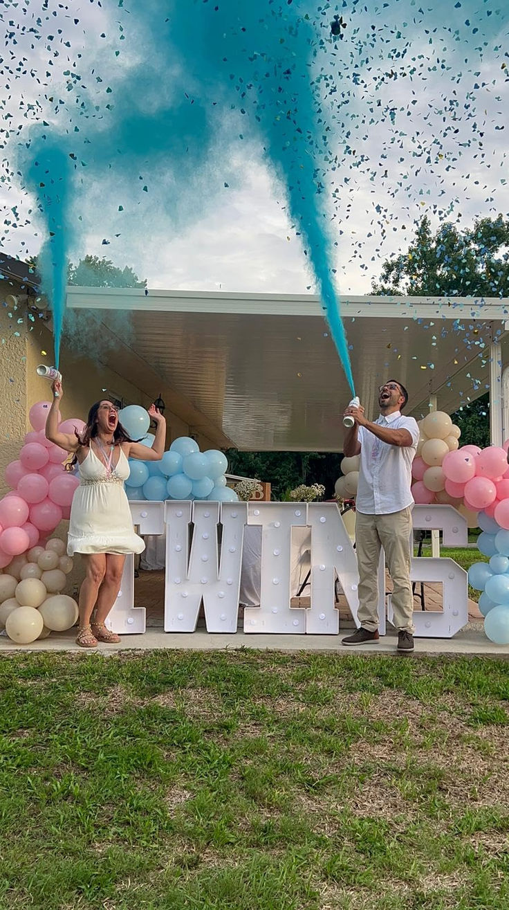 two people standing in front of a sign with balloons and streamers