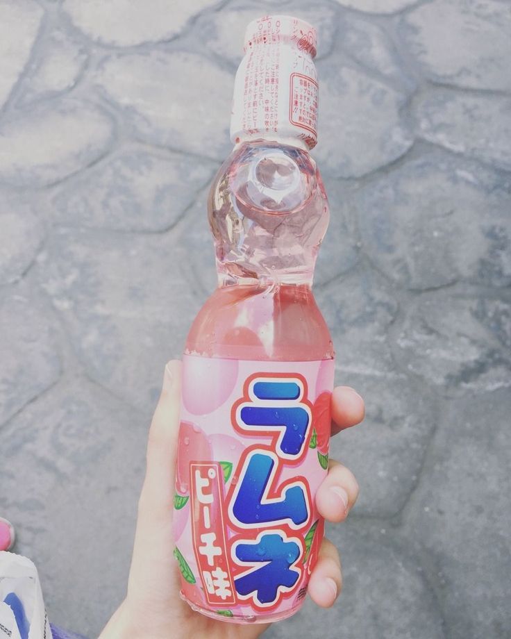 a person holding up a pink soda bottle with japanese writing on the top and bottom