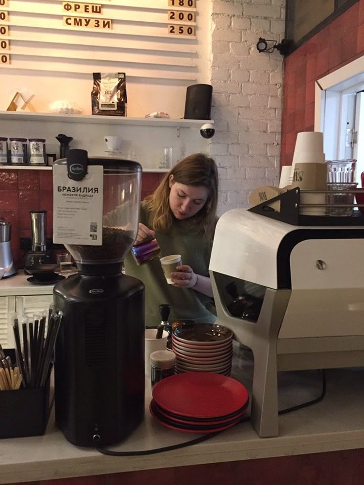 a woman pouring coffee into a blender at a counter in a cafe with plates, cups and utensils on it